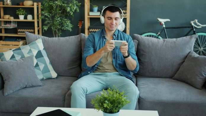 Man wearing headphones plays game on smartphone on phone.