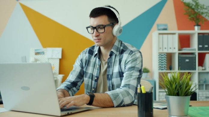 Man wearing headphones works on a laptop.