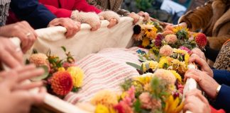 People carry a flower-covered wicker casket.