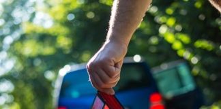 Close-up of a hand placing an emergency warning triangle by a car.