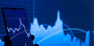 a person holding a cell phone in front of a stock chart