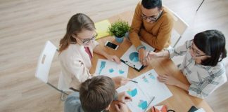 Four people collaborating around a table with charts.