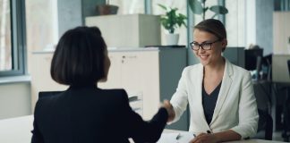 Two women shaking hands across a desk