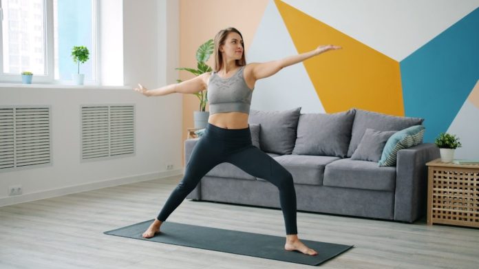 Woman practicing warrior ii pose on yoga mat.