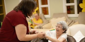 Caregiver assists elderly woman with walker.