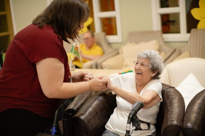 Caregiver assists elderly woman with walker.
