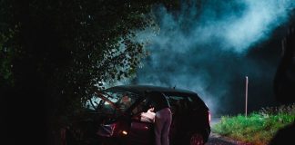 a person standing next to a car with smoke coming out of it