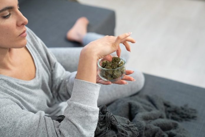 a woman sitting on a couch holding a bowl of marijuana
