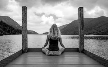 A woman sitting on a dock in front of a body of water