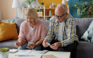 Elderly couple reviews finances at home on couch.