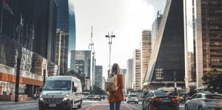 photography of woman walking in between road with vehicles