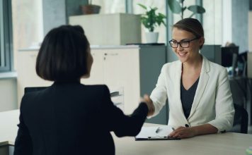 Two women shaking hands across a desk