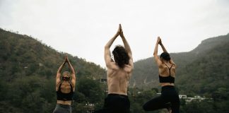 three people doing yoga on a rock near a river