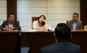 Courtroom Drama vs. Courtroom Reality: What Legal Series Get Right and Wrong About Criminal Defense A person in a suit facing three people seated at a long wooden table