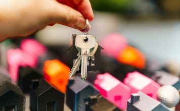 Hand holding house keys over miniature houses