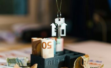 A house hanging from a string on top of a pile of money
