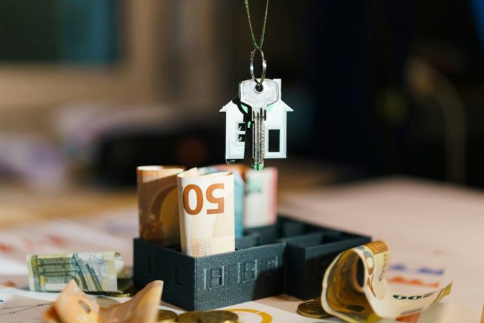 A house hanging from a string on top of a pile of money